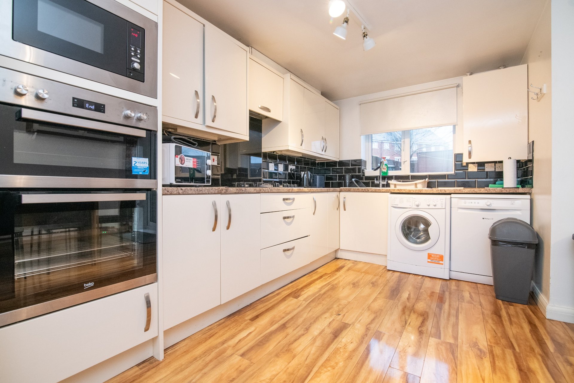 Modern kitchen with white cabinetry, wooden flooring, integrated appliances and washing machine
