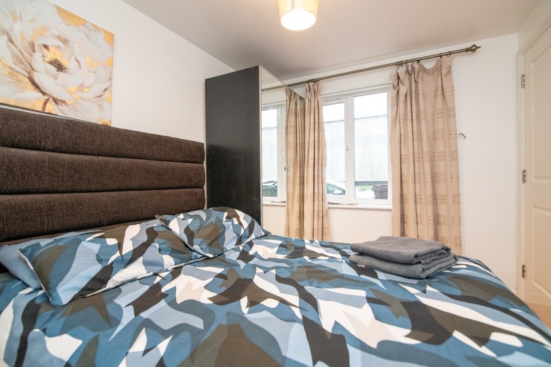 Modern bedroom with double bed, patterned duvet, brown padded headboard and window with curtains