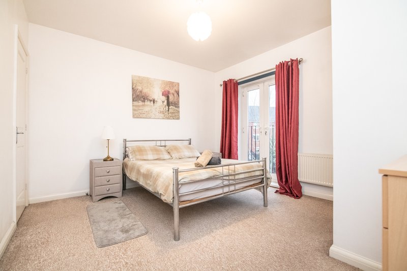 Bright bedroom with metal-frame bed, beige bedding, red curtains, and wooden nightstand