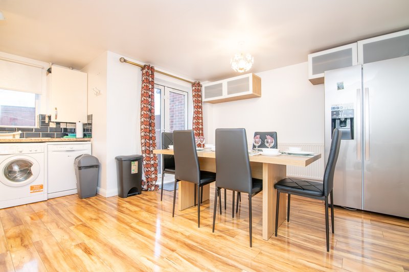 Open-plan kitchen-diner with wooden flooring, dining table, chairs, and integrated appliances