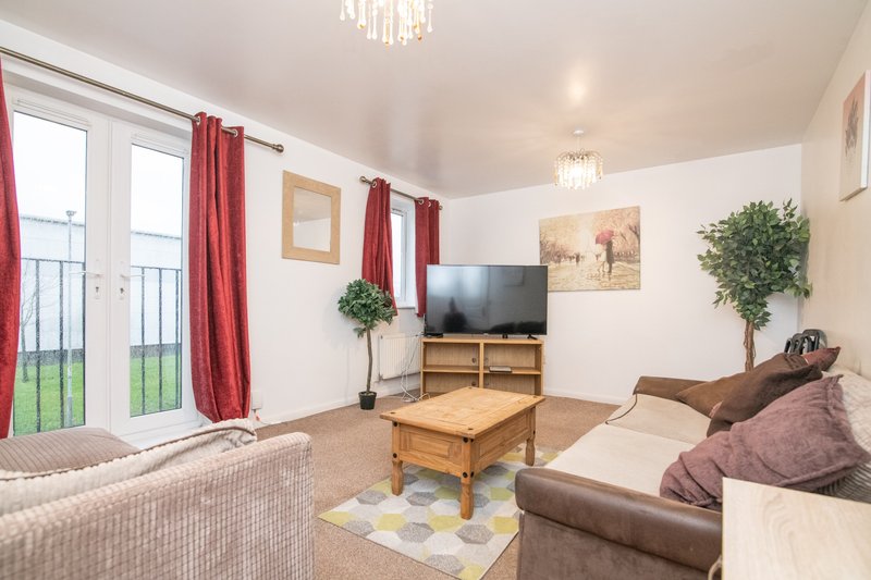 Bright living room with sofa, wooden coffee table, TV, red curtains and patio doors
