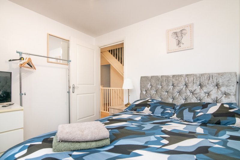 Bedroom with double bed, blue patterned duvet, grey headboard, wooden staircase and white walls