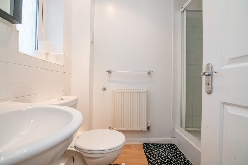 Clean bathroom with toilet, sink, radiator, shower cubicle and wooden floor
