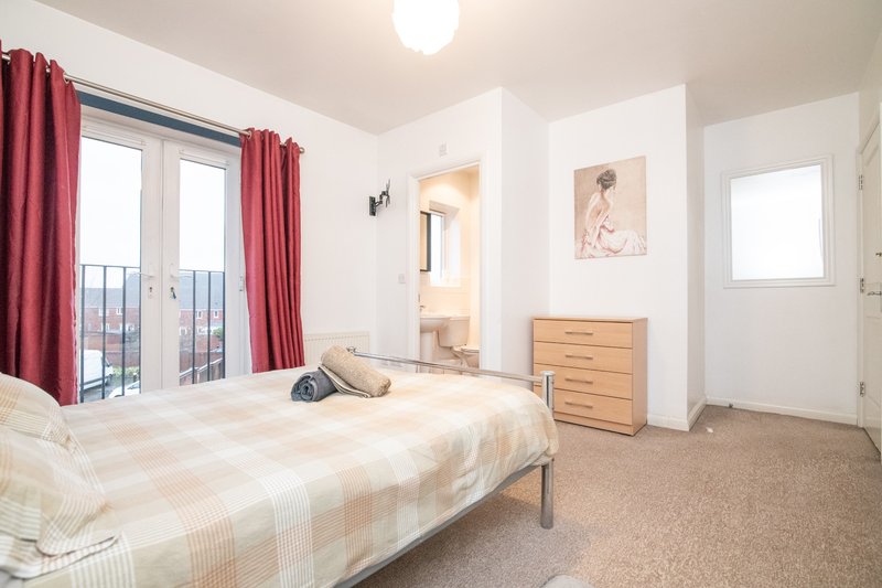 Bright bedroom with double bed, red curtains, wooden chest of drawers and balcony access