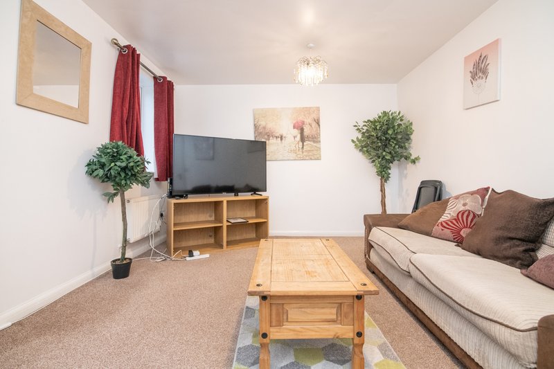 Living room with sofa, wooden coffee table, TV stand, potted plants and red curtains