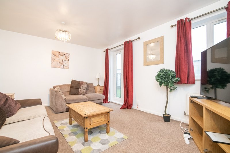 Bright living room with brown sofa, wooden coffee table, TV, red curtains and potted plant