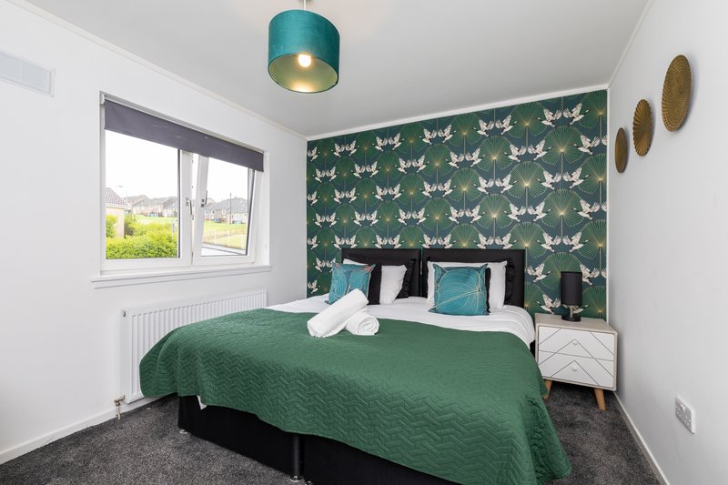 Bedroom with double bed, green quilted bedding, patterned wallpaper and pendant light