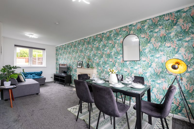Open-plan living and dining area with patterned wallpaper, dining table, sofa and yellow floor lamp