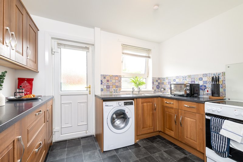Modern kitchen with wooden cabinets, washing machine, and tiled backsplash