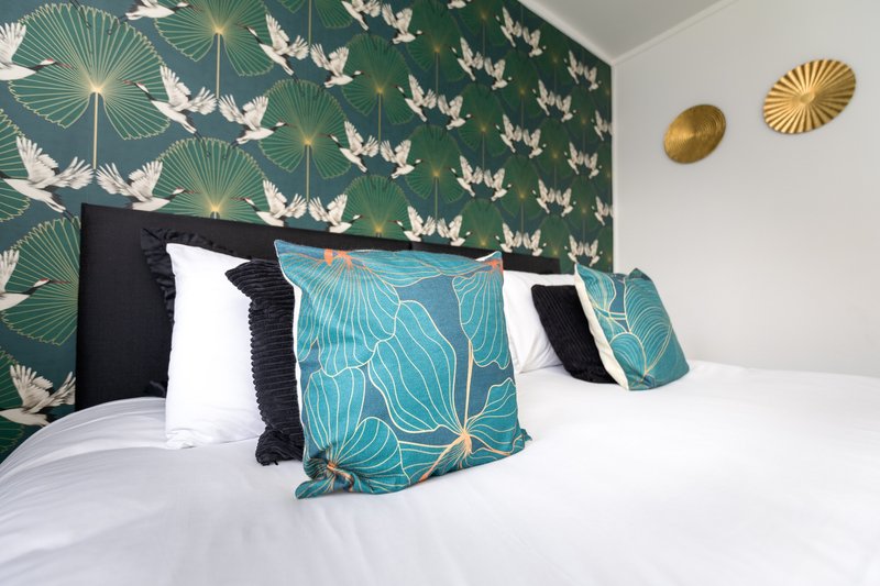 Bedroom with patterned teal accent wall, white bedding, decorative pillows and gold wall decor