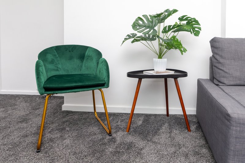 Living room with green velvet armchair, small round side table with potted plant, and gray sofa