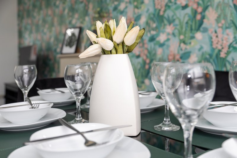 Formal dining table setting with white plates, glassware, and white vase of tulips