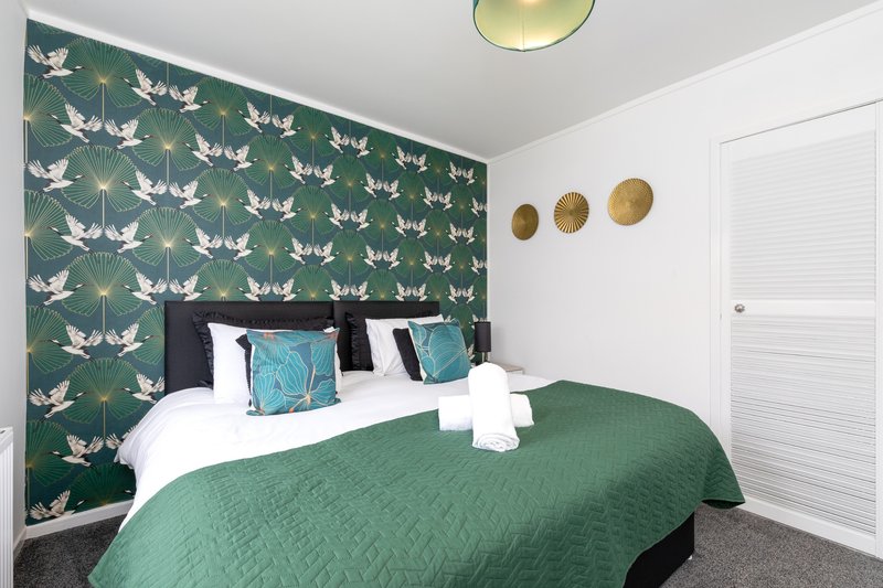 Bedroom with green patterned accent wall, double bed, white pillows and green bedding
