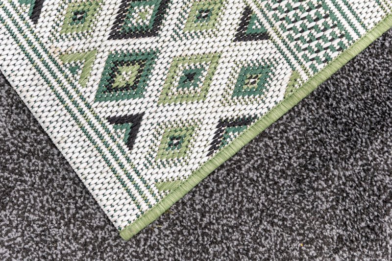 Close-up of patterned area rug with green and cream geometric design on carpeted floor