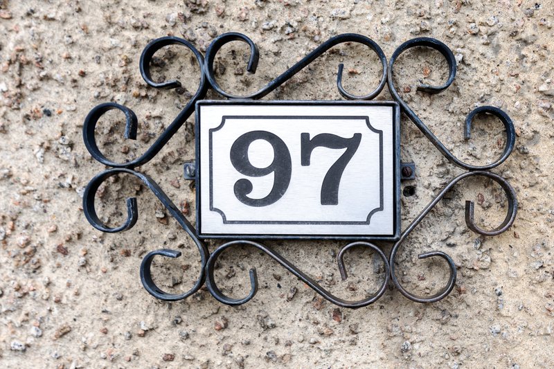 Decorative house number 97 mounted on textured stone wall