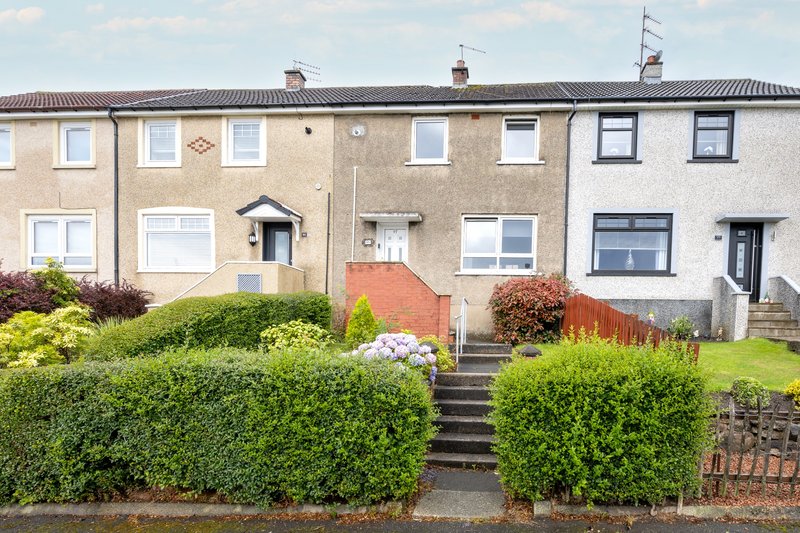 Terraced residential houses with front gardens, hedges, and brick boundary wall
