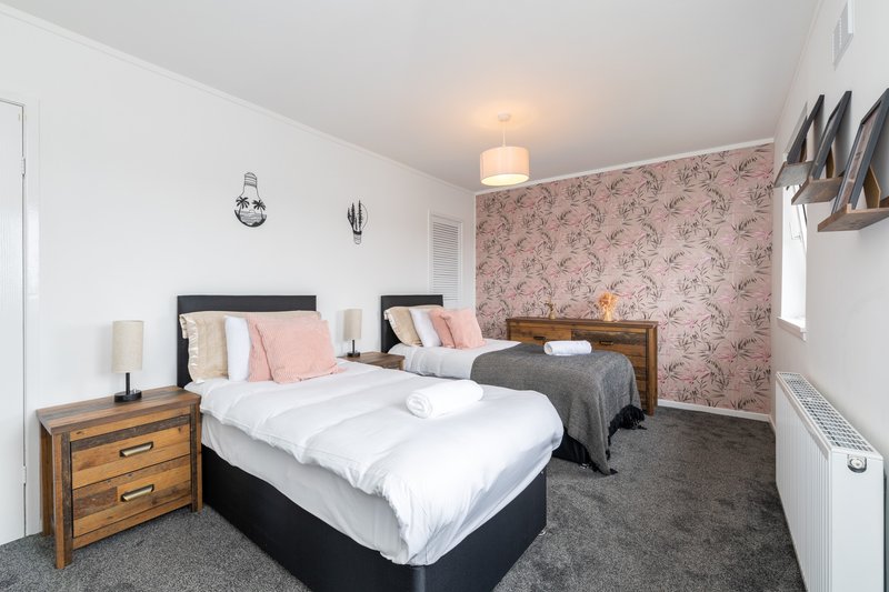 Bright bedroom with two double beds, wooden nightstands, floral wallpaper and shared bathroom access