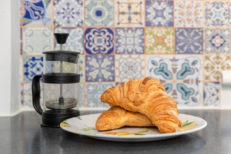 Kitchen counter with croissants on plate, french press, and decorative tile backsplash