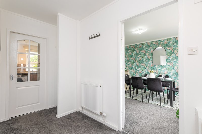 Hallway with white walls, grey carpet, and doorways leading to dining area and kitchen