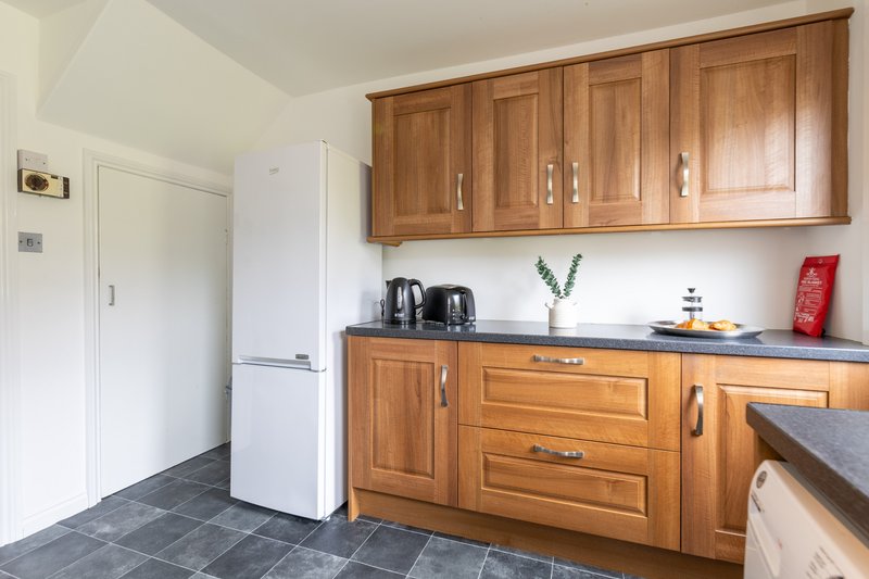 Modern kitchen with wooden cabinetry, dark countertops, white refrigerator and slate flooring