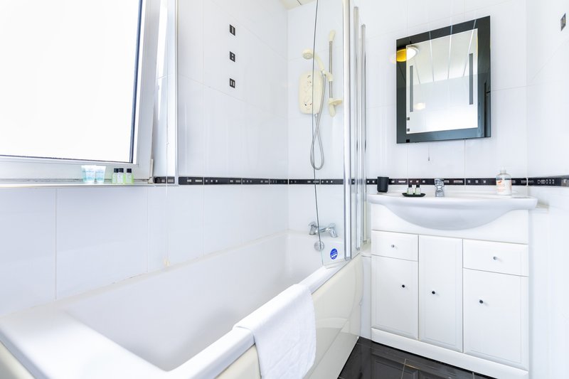 Clean modern bathroom with white bathtub, pedestal sink, mirror and black tile trim