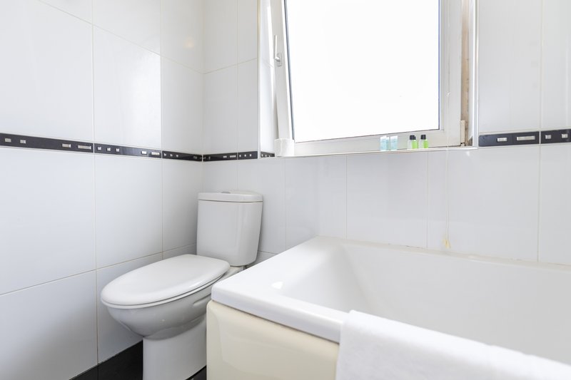 Clean bathroom with toilet, white bathtub, mirror and window with natural light