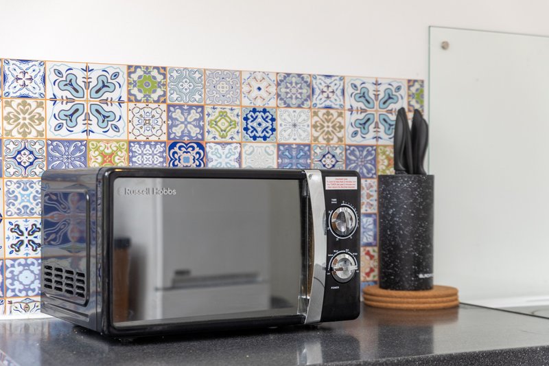 Kitchen countertop with microwave, decorative tile backsplash, and utensil holder