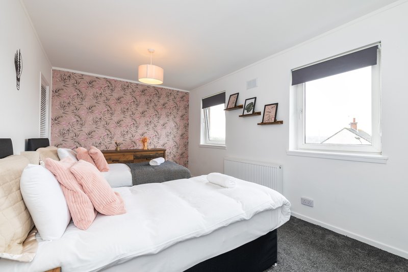 Bright bedroom with double bed, pink patterned headboard, white bedding and windows