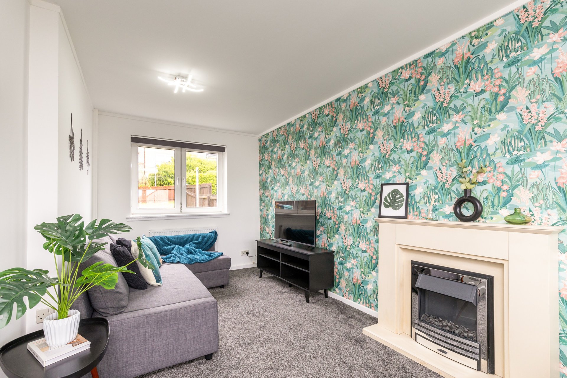 Modern living room with gray sofa, tropical wallpaper, fireplace and window