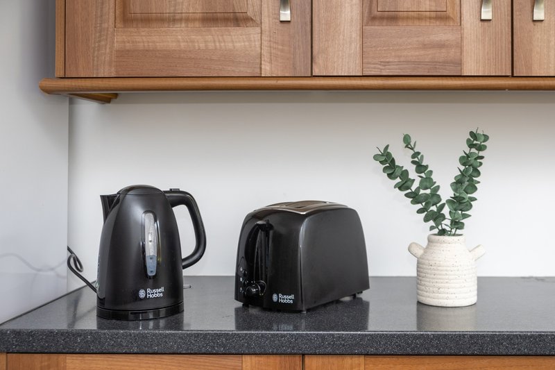 Kitchen countertop with black kettle, toaster, potted plant and wooden cabinets above
