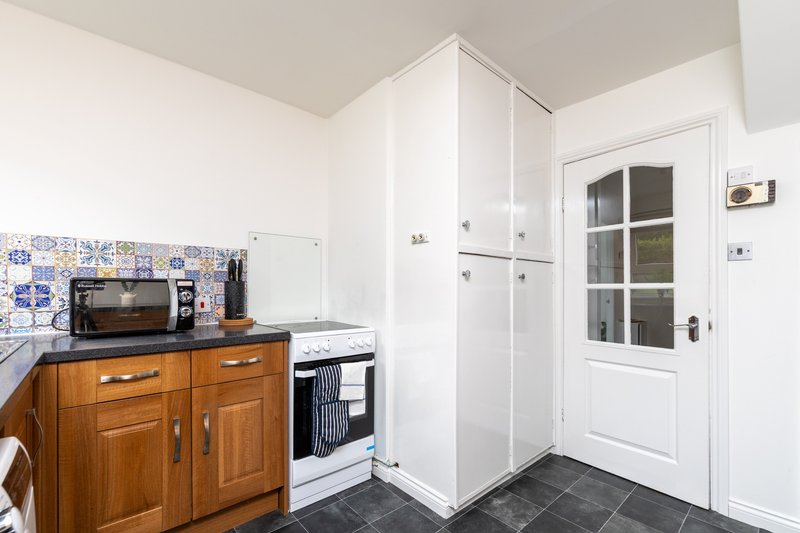 Kitchen with wooden cabinets, electric oven, blue tile backsplash and white corner cupboard