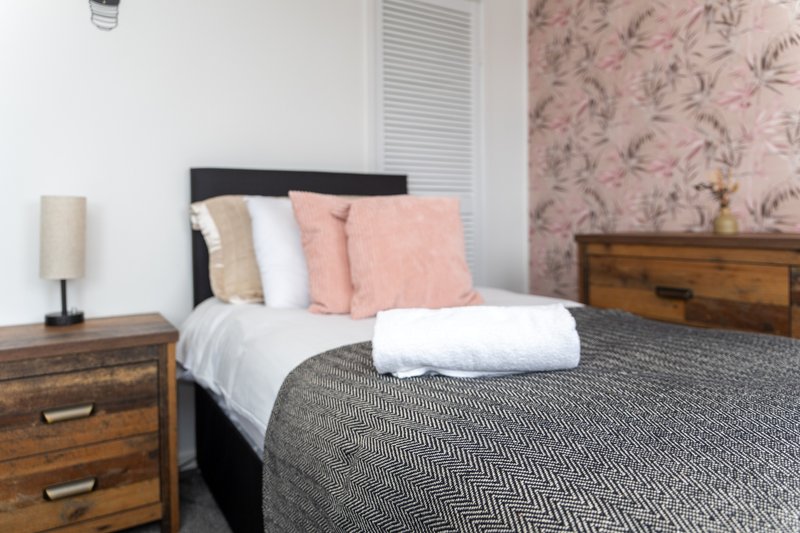 Bedroom with double bed, pink cushions, wooden bedside tables and floral wallpaper