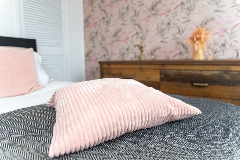 Bedroom with double bed, pink and grey bedding, wooden dresser and floral wallpaper