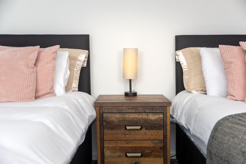 Twin bedroom with two beds, wooden nightstand, lamp, and pink decorative pillows