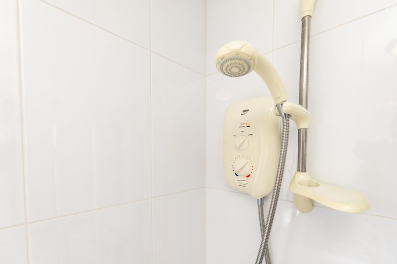 White bathroom with electric shower unit, showerhead and chrome fixtures
