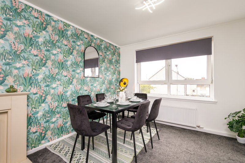 Modern dining room with black table, upholstered chairs, floral wallpaper and large window