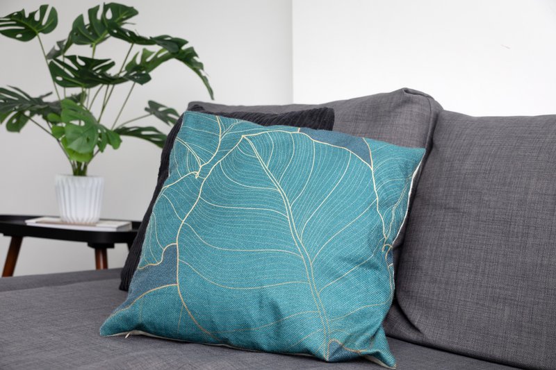 Grey sofa with turquoise patterned cushion, potted plant and side table