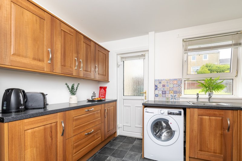 Kitchen with wooden cabinets, black countertops, washing machine, and window overlooking garden