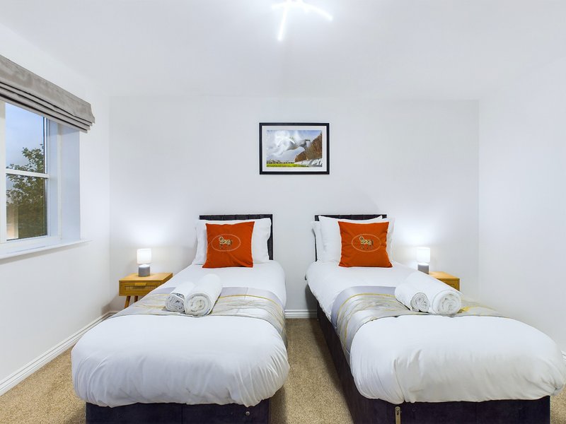 Twin bedroom with white bedding, orange cushions, wooden nightstands, and window with natural light