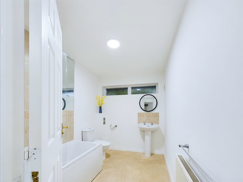 Modern bathroom with white cabinetry, pedestal sink, bathtub, and beige floor tiles