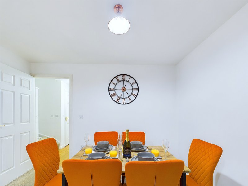 Bright dining room with orange chairs, set table, wall clock and ceiling light