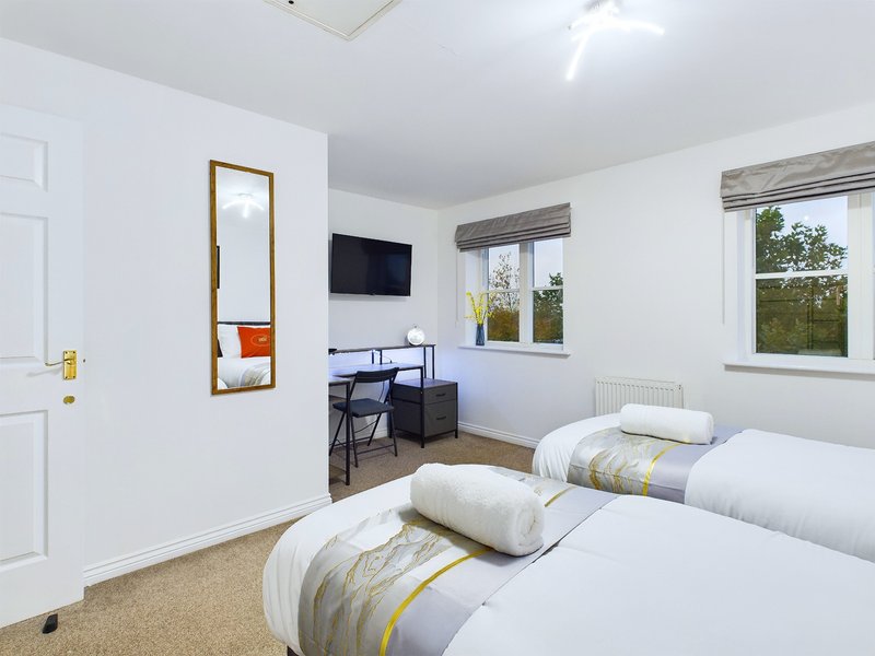 Bright bedroom with two single beds, desk, mirror, wall-mounted TV and windows