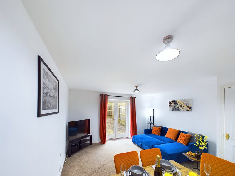 Bright living room with blue sofa, orange chairs, TV, and natural light from patio doors