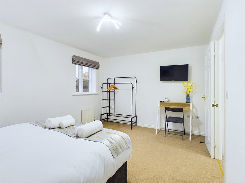 Bright bedroom with double bed, desk, TV, clothing rack and window