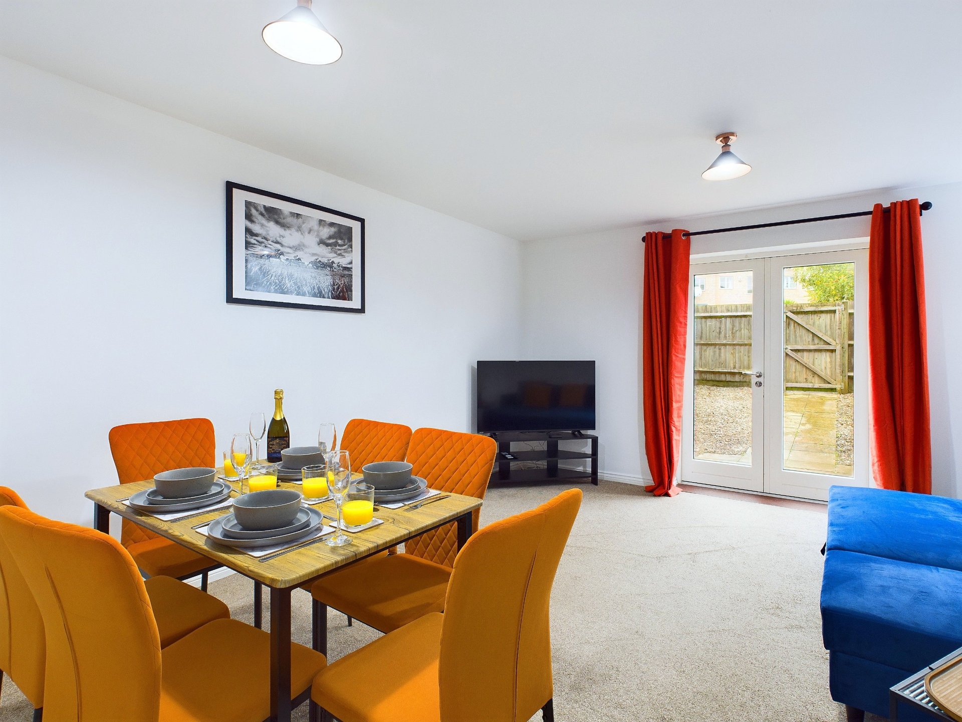 Open-plan living and dining area with orange chairs, dining table, TV, and red curtains