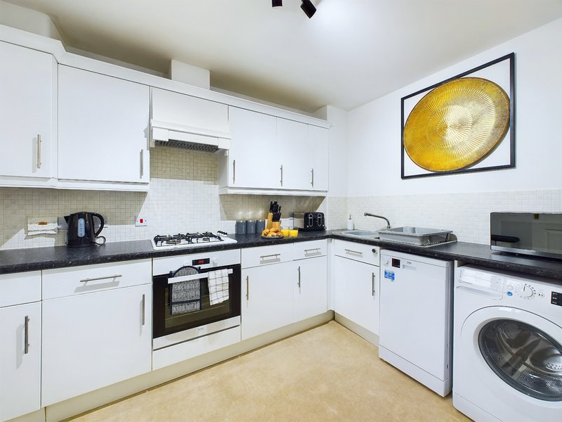 Modern white kitchen with black countertops, gas hob, built-in appliances and washing machine