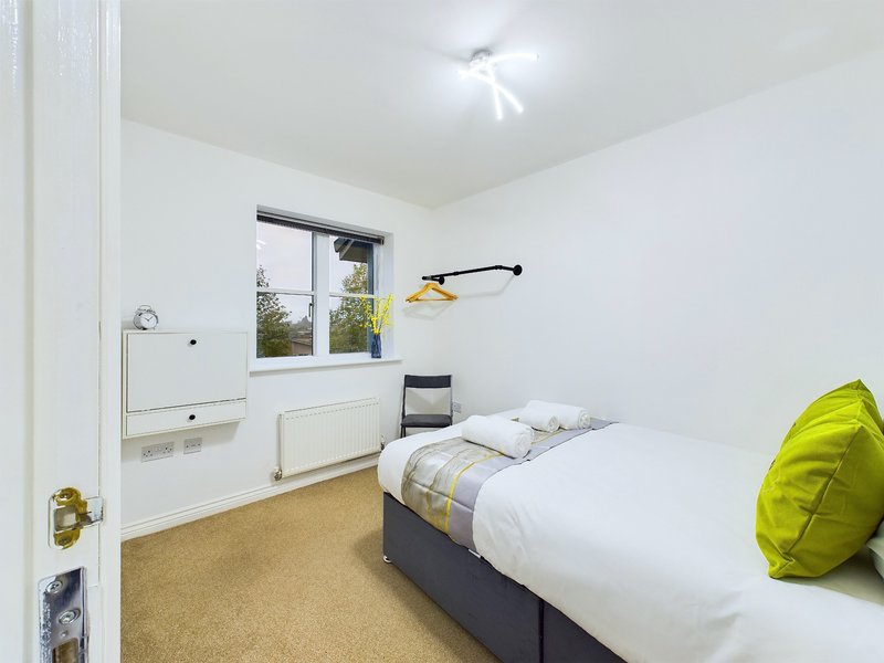 Bright bedroom with single bed, built-in storage, window, and yellow accent cushion