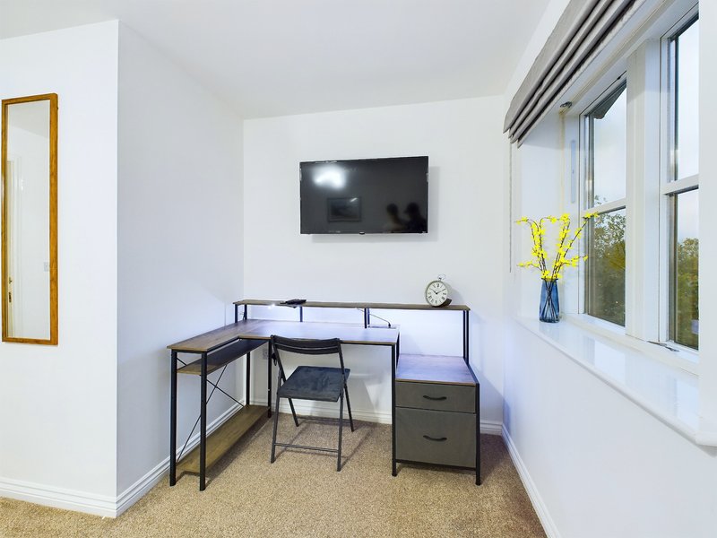 Bright bedroom corner with desk, chair, wall-mounted TV, and large windows