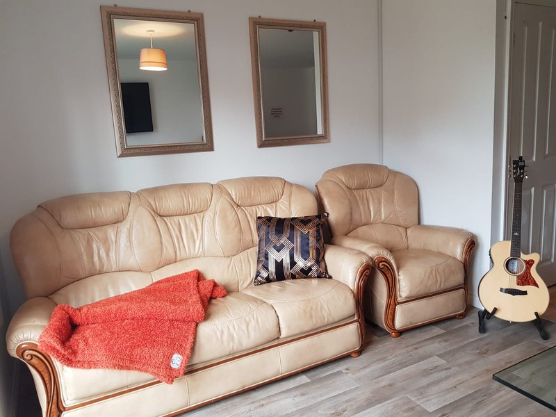 Living room with tan leather sofa, armchair, red throw blanket, acoustic guitar, and wall mirrors