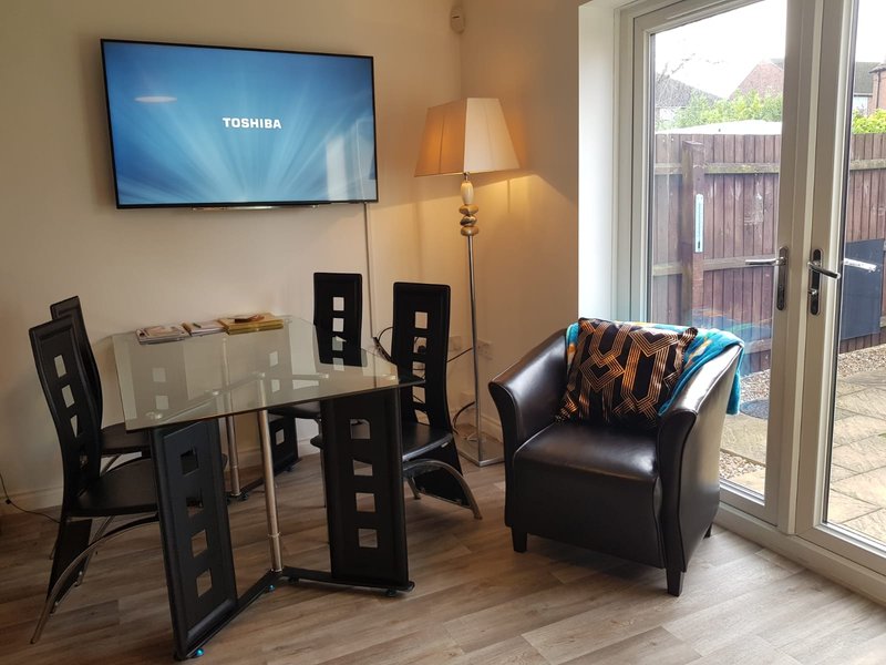 Living room with wall-mounted TV, black leather armchair, dining table, chairs and patio doors